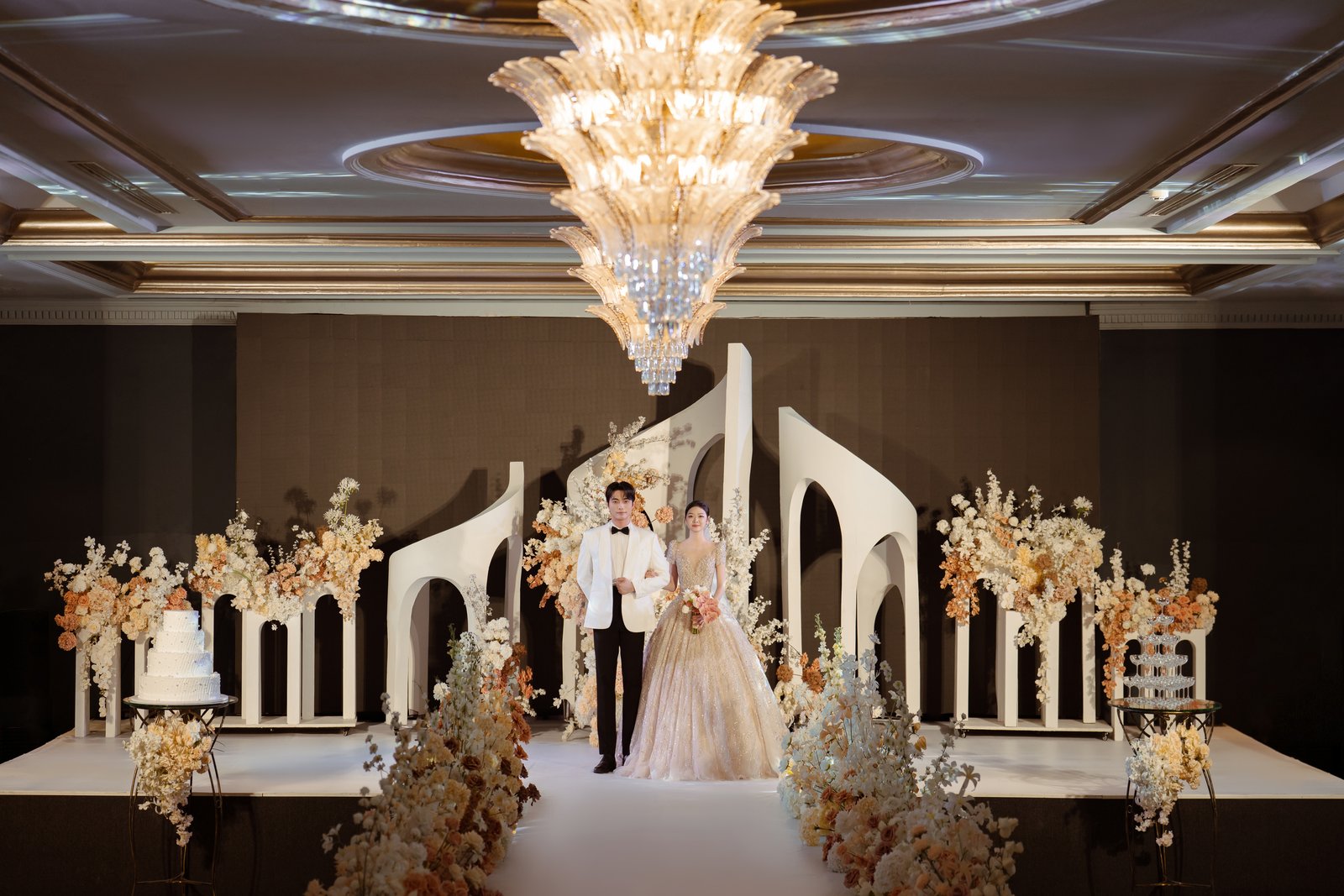 Cô dâu chú rể trên sân khấu sảnh Queen dưới đèn chùm pha lê